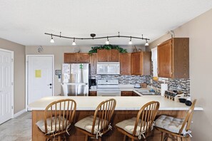 A kitchen with wooden cabinets, a stainless steel refrigerator, a microwave, a stove, and a bar area with wooden chairs. - Southwood Shores 217-1A (Village of Four Seasons)