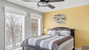 Un dormitorio con una cama, un ventilador de techo, un reloj de pared y una decoración de peces en la pared.