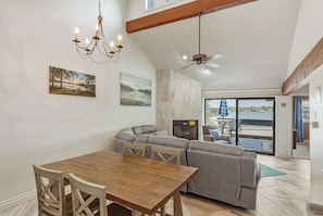 A dining area with a wooden table and chairs, a gray sofa, a chandelier, a ceiling fan, and a view of the outdoors through a glass door. - Knolls 0634 - Two Bedroom Apartment, Sleeps 6 (Osage Beach)