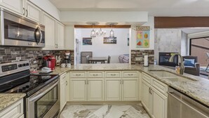 Una cocina con armarios blancos, microondas, estufa y comedor con mesa y sillas.