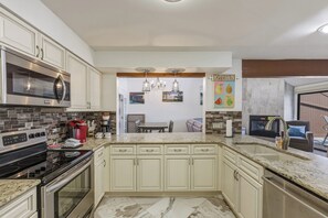 A kitchen with white cabinets, a microwave, a stove, and a dining area with a table and chairs. - Knolls 0634 - Two Bedroom Apartment, Sleeps 6 (Osage Beach)