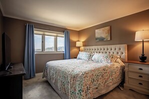 A bedroom with a bed, a television, a window with curtains, a bedside lamp, and a painting on the wall. - Knolls 0634 - Two Bedroom Apartment, Sleeps 6 (Osage Beach)