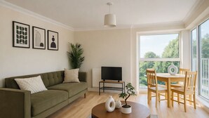 A modern living room with a green sofa, a round coffee table with decorative items, a TV, and a dining area with wooden chairs. - Modern 2-bed Apartment Near Wembley Stadium (Wembley)
