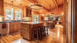 A spacious kitchen with wooden cabinets, a large island with stools, and a stone fireplace. - Lockout -Reduced Bedrooms - Four Season, Lakefront, Sandy Beach, Amazing Sunsets (Saranac Lake)