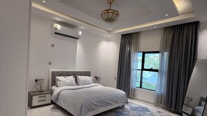 Quarto moderno com uma cama grande, iluminação no teto, ar condicionado e vista para o exterior pela janela.