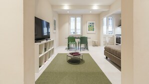 Ein modernes Wohnzimmer mit Flachbildfernseher, grünen Sesseln, einem Esstisch und einer Couch.