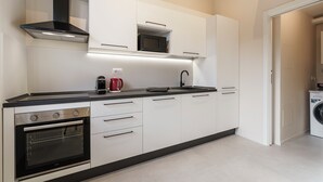Een moderne keuken met witte kastjes, een zwart aanrecht, een ingebouwde oven, een magnetron, een koffiezetapparaat en een spoelbak.