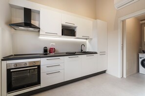 A modern kitchen with white cabinets, a black countertop, a built-in oven, a microwave, a coffee maker, and a sink. - Palazzo Accademia-Giotto-4 (Firenze)