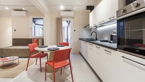 A modern kitchen with white cabinets, a black countertop, and a built-in oven. There is a dining area with a round table and red chairs. - Palazzo Accademia-Michelangelo-5 (Firenze)