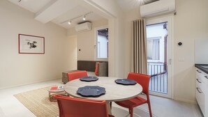 A modern dining area with a round table, red chairs, and a light-colored floor. - Palazzo Accademia-Michelangelo-5 (Firenze)