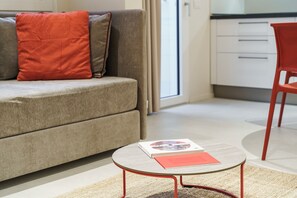 Een moderne woonkamer met een grijze bank, rode kussens, een klein rond tafeltje met een boek, en een rode fauteuil.