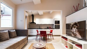 A modern living room with a sofa, a coffee table, a TV, and a dining area with chairs and a table. - Palazzo Accademia-Michelangelo-5 (Firenze)