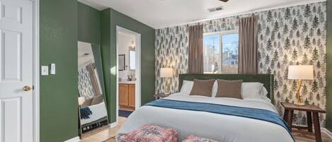 Une chambre à coucher comprenant un lit, deux tables de chevet, un ventilateur de plafond et une fenêtre avec des rideaux.