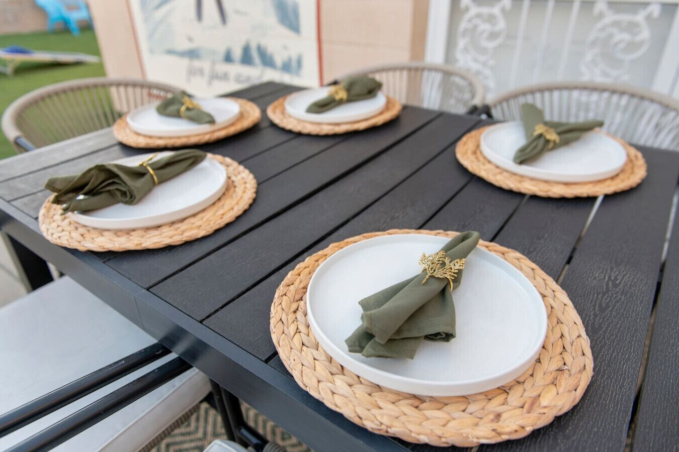 Una mesa dispuesta con platos blancos, servilletas verdes y individuales tejidos.