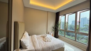 A modern hotel room with a large bed, a bedside table, a lamp, and a view of the city through large windows. - Dorsett Hartamas|KL City|Rooftop Pool|Bathtub|1KM from 1Mont Kiara|8KM from KLCC (Kuala Lumpur)