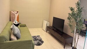 A living room with a green sofa, a black TV on a stand, a small plant, and a painting on the wall. - Dorsett Hartamas|KL City|Rooftop Pool|Bathtub|1KM from 1Mont Kiara|8KM from KLCC (Kuala Lumpur)