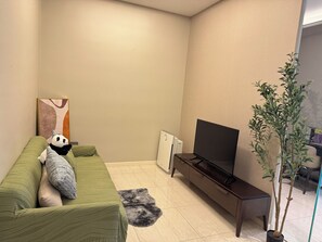 A living room with a green sofa, a black TV on a stand, a small plant, and a painting on the wall. - Dorsett Hartamas|KL City|Rooftop Pool|Bathtub|1KM from 1Mont Kiara|8KM from KLCC (Kuala Lumpur)