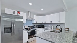 Una cocina moderna con armarios blancos, electrodomésticos de acero inoxidable, encimeras de granito y horno empotrado.