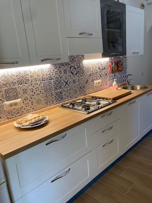 A kitchen with white cabinets, a patterned backsplash, a gas stove, and a sink.