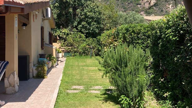 A house with a tiled patio, a small garden, and a view of a mountain. - Cozy house with garden on two sides 350m from the sea (Costa Rei)
