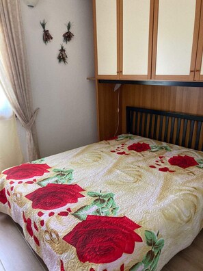 A bedroom with a bed covered in a floral quilt, a wooden headboard, and a wall with three wall-mounted decorations.