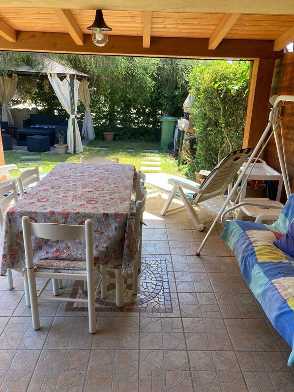 A covered patio area with a table and chairs, a cushioned bench, and a pergola with curtains.