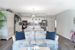 A modern living room with a sofa, a coffee table, and a dining area in the background. - Colony By the Sea 106, Oceanside Condo in Salter Path NC (Salter Path)