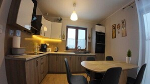 A compact kitchen with wooden cabinets, a dining table with chairs, and a hanging light fixture. - Large, comfortable holiday home, private garden (Debina)