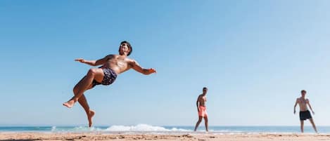 Een strandscène met iemand die springt om een bal te vangen.