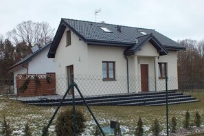 Une maison à deux étages avec un toit en pente, une cour clôturée et un petit escalier menant à l’entrée.
