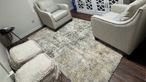 Una sala de estar con dos sillones, una mesa de centro, una alfombra, un aparador con objetos decorativos y un cuadro en la pared.