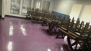Una habitación con piso morado, ventiladores de techo y filas de sillas de madera.