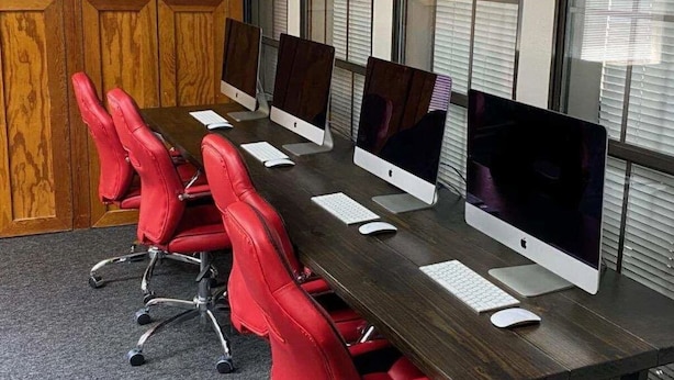 Una sala de conferencias con una mesa larga, sillas rojas y computadoras Apple iMac.