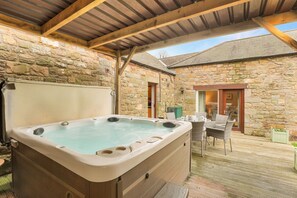 Edificio de piedra con jacuzzi, mobiliario exterior y techo de madera.