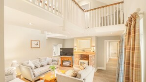 Ein geräumiges Wohnzimmer mit hohen Decken, einem Kamin, einem Fernseher und einer Treppe zu einer oberen Ebene.