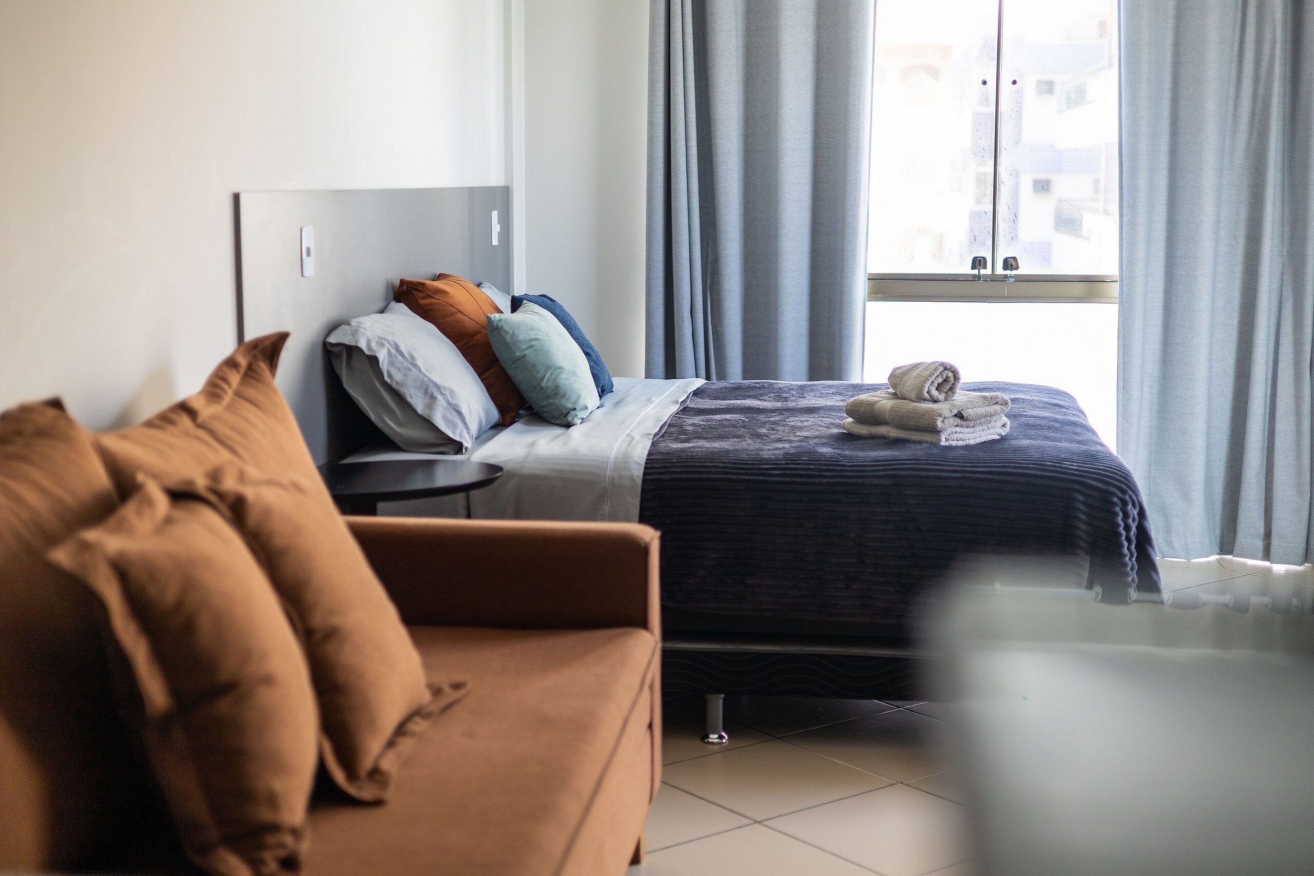 Een hotelkamer met een bed, een slaapbank, een raam met gordijnen en uitzicht op gebouwen.