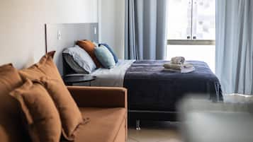 Une chambre d’hôtel avec un lit, un canapé, une fenêtre avec des rideaux et une vue sur les bâtiments environnants.
