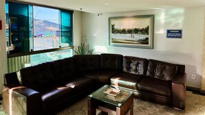 A living area with a large window, a brown leather sofa, a glass coffee table, and a painting on the wall. - Loft equipado a poucos passos da praia (Arraial do Cabo)