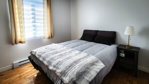 Ein Schlafzimmer mit einem Bett, einem Nachttisch, einer Lampe und einem Fenster mit Vorhängen.