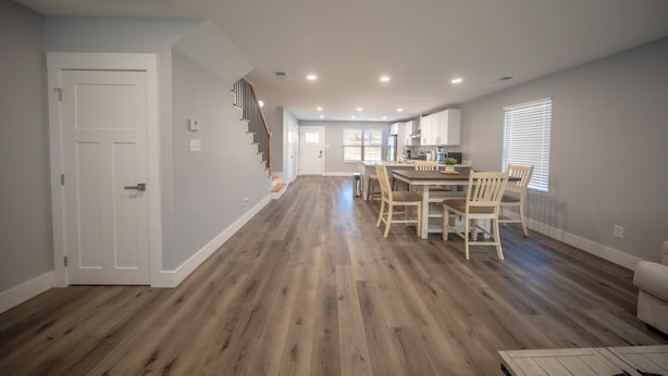 A spacious living area with hardwood flooring, a dining table with chairs, a staircase, and a kitchen area with cabinets and a window. - Stadium, mall,civic center, dining, shopping (Knoxville)