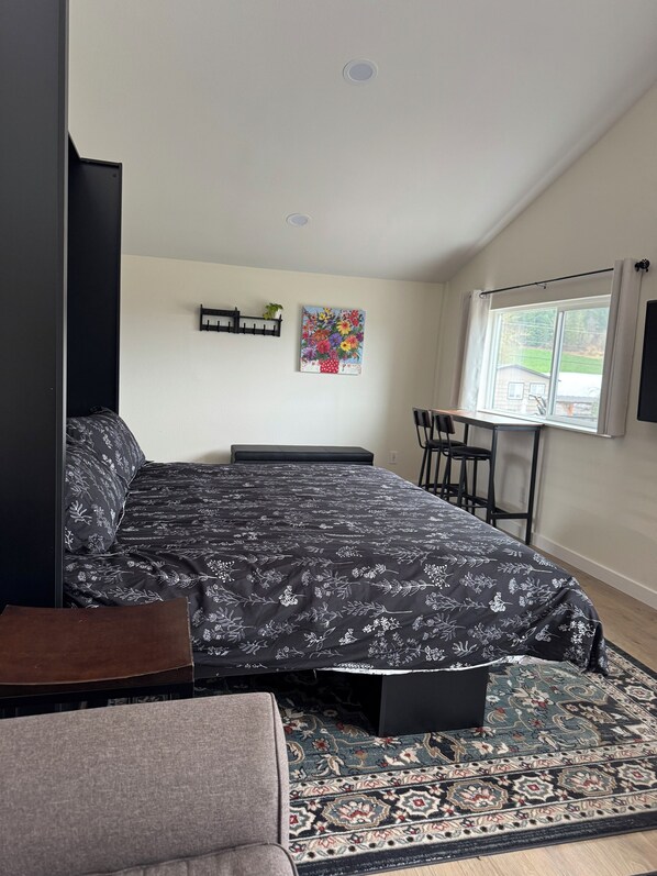 A bedroom with a bed, a desk, a chair, a rug, and a window with a view.