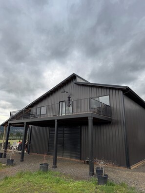 A large, dark-colored barn with a balcony and a covered area.