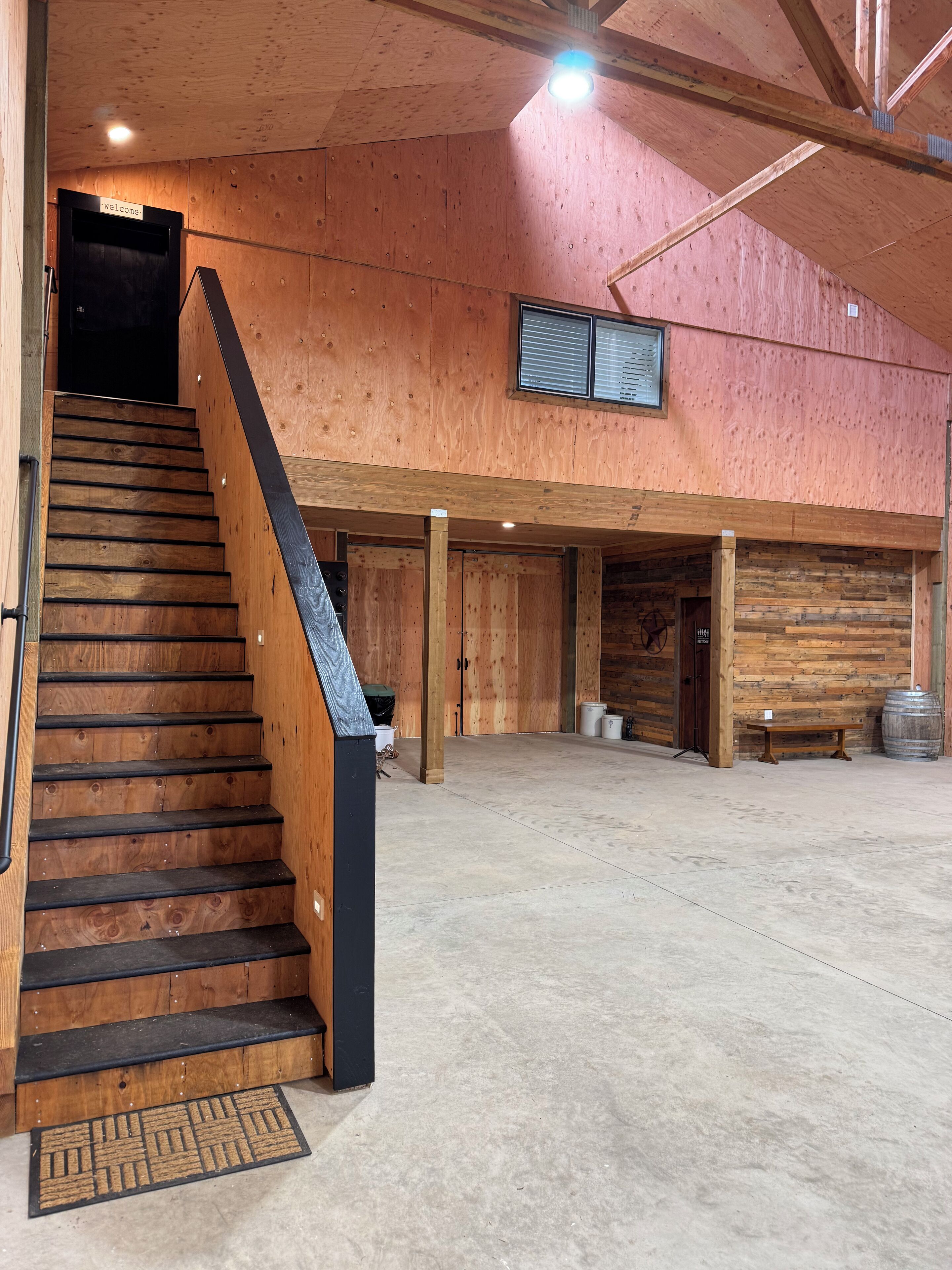 A wooden staircase leading to a room with a 'Welcome' sign, a bench, and a barrel.
