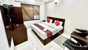 A hotel room with a bed, a desk, a chair, a ceiling fan, and a window with blinds. - Hotel Siam International Karol Bagh New Delhi (New Delhi)
