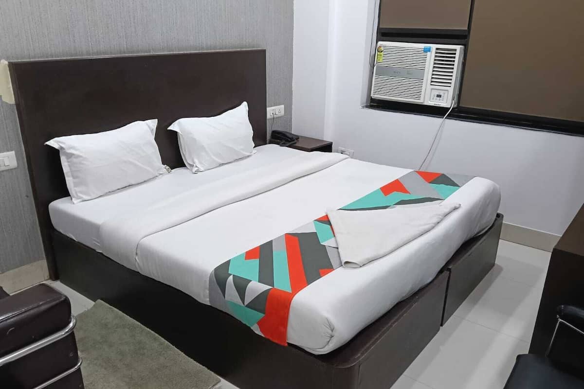 A hotel room with a bed, a nightstand, an air conditioning unit, and a desk.