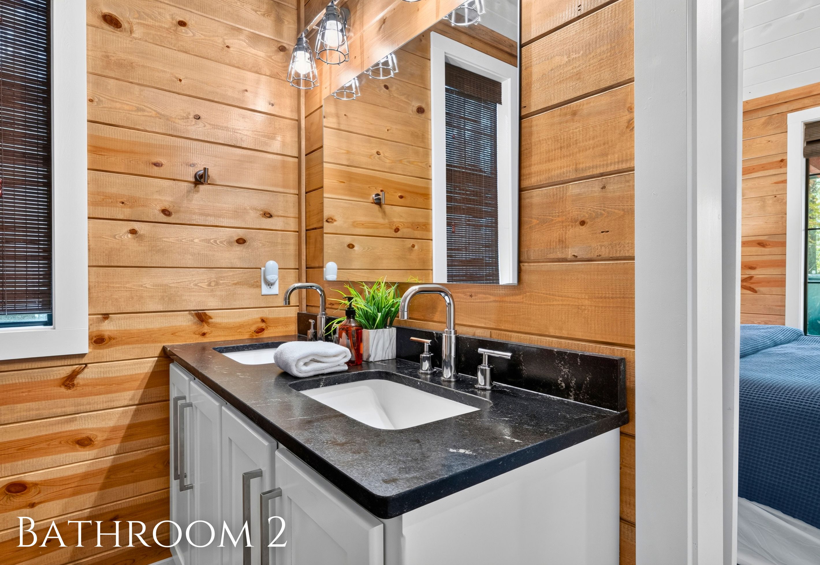 A bathroom with wooden paneling, a double sink, a mirror, and a window with blinds.