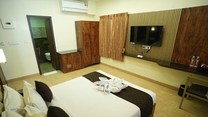 Quarto de hotel com cama, televisão, guarda-roupa e casa de banho visível por uma porta aberta.