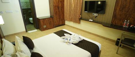 A hotel room with a bed, a TV, a wardrobe, and a bathroom visible through an open door.