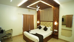 Quarto de hotel com uma cama grande, uma escrivaninha com cadeira, um ventilador de teto e um espelho na parede.
