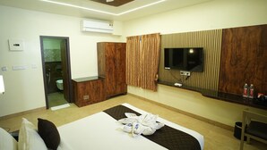 Quarto de hotel moderno com cama, televisão fixada na parede, guarda-roupa de madeira e casa de banho visível através de uma porta aberta.
